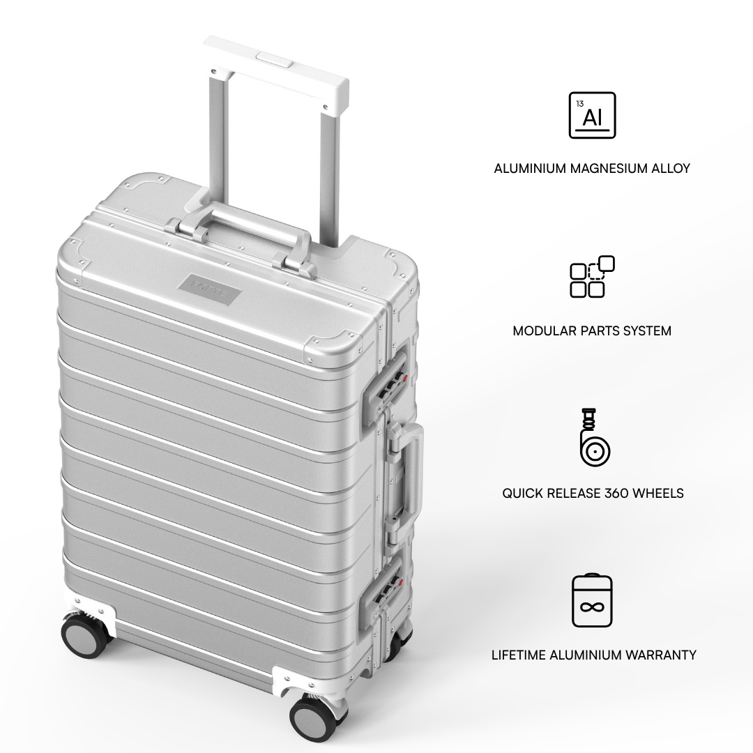 A silver aluminium rolling suitcase with an extended telescopic handle and four spinner wheels, shown on a light gray background with feature callout icons and text describing its materials, modular design, wheels, and warranty.